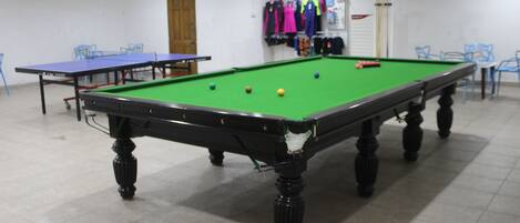 Une table de billard avec des billes, une table de ping-pong et des chaises dans une pièce dont le sol est recouvert de carreaux.