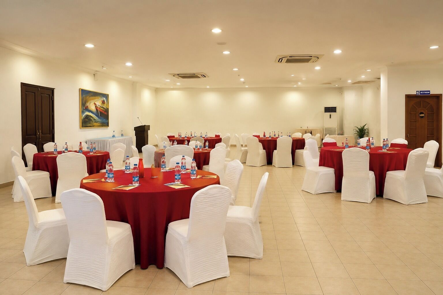 Une salle de conférence avec des tables rondes, des chaises blanches et des nappes rouges.