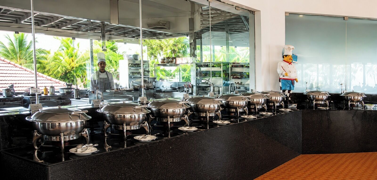 Montaje tipo bufé con varias estaciones de servicio, un cocinero y vistas tropicales al aire libre.