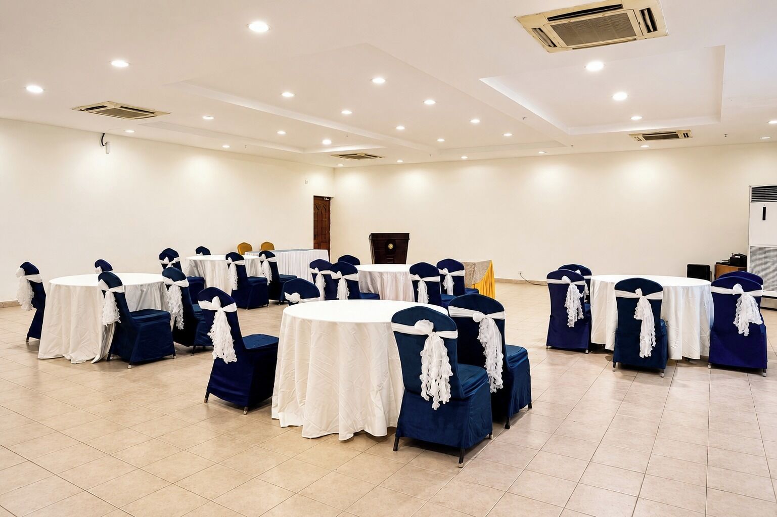 A conference room with round tables and chairs, white tablecloths, and blue chairs with white sashes.