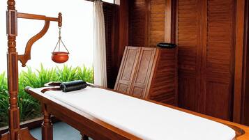 Una mesa de masaje de madera con sábana blanca, cojín negro y reposapiés de madera.