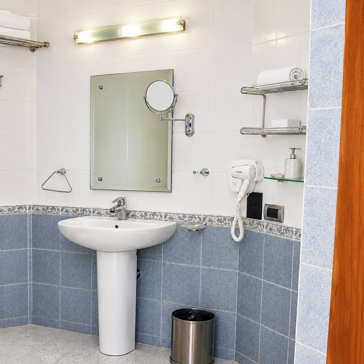 Un baño con lavamanos, espejo, toallero y secador de pelo en una estantería.
