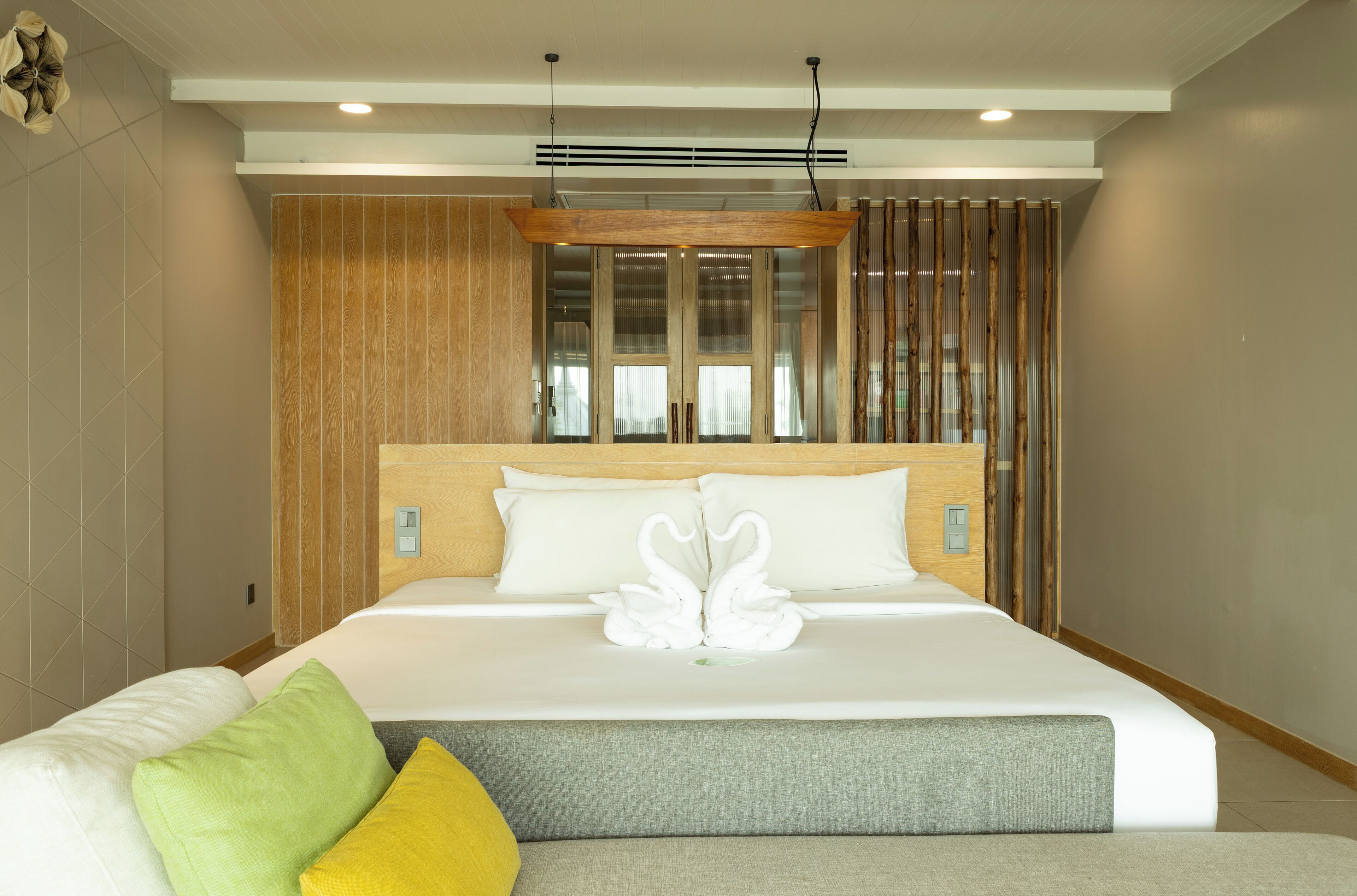 A modern hotel room with a large bed, a wooden headboard, and a view through a window with vertical blinds.