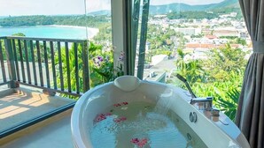 A modern bathroom with a large bathtub, a balcony with a view of the sea and greenery, and a large window. - Andaman Cannacia Resort & Spa (Karon)