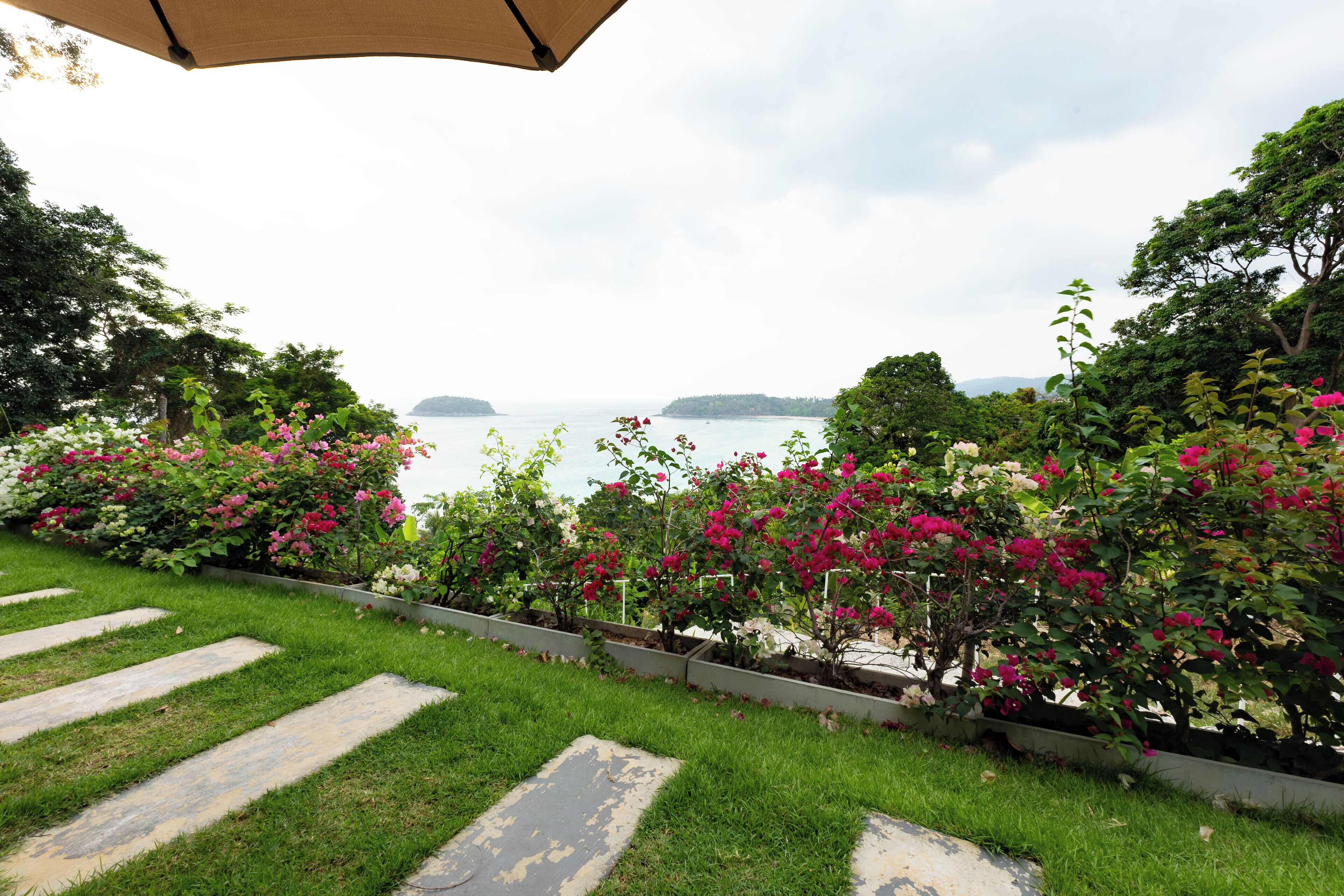 Un jardin avec un sentier de pierres qui mène à un point de vue sur la mer et les îles lointaines.