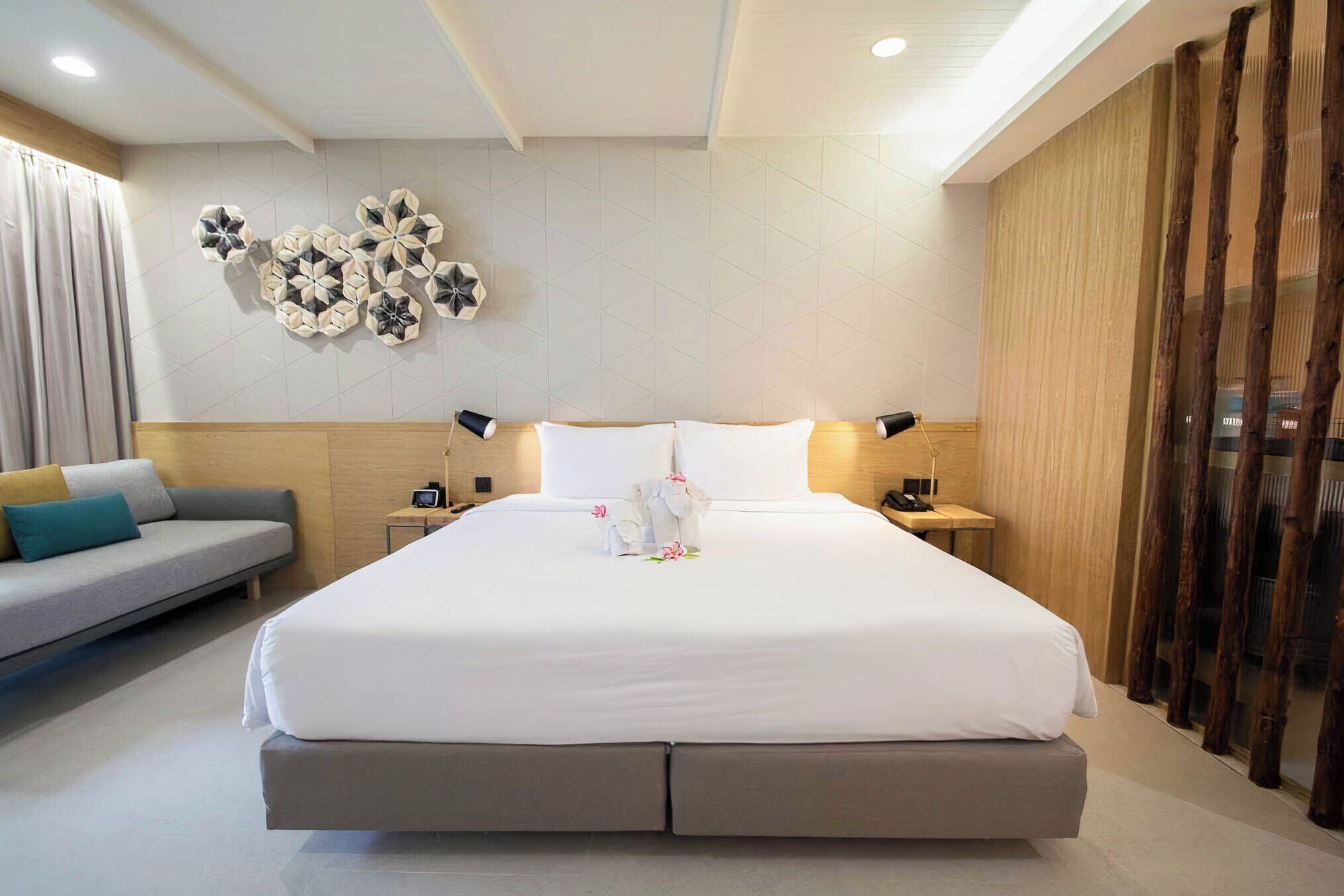 A modern hotel room with a large bed, a sofa, and decorative wall art.