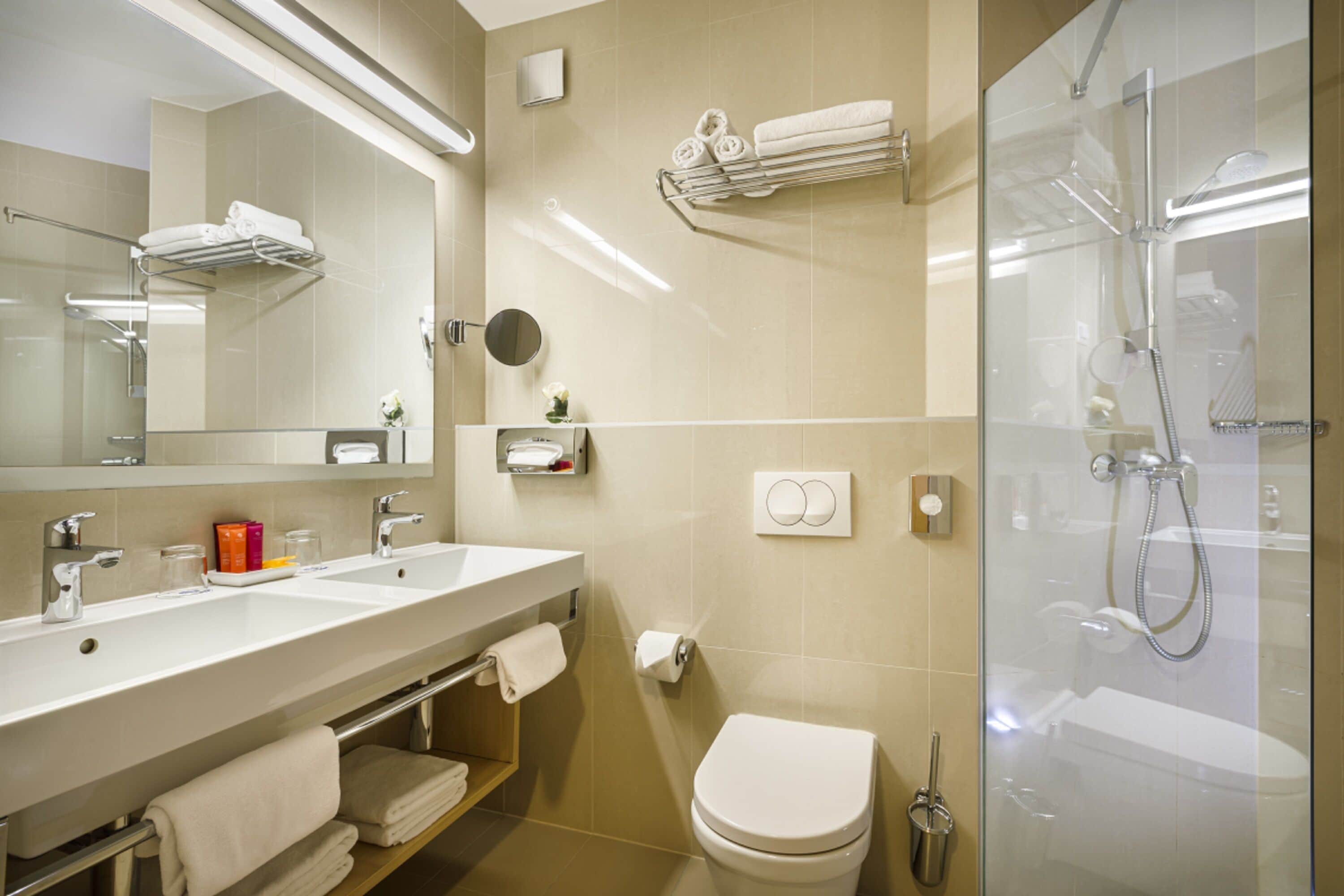 Un baño moderno con tocador de doble lavabo, inodoro, cabina de ducha con mampara de vidrio y espejo sobre el lavabo.