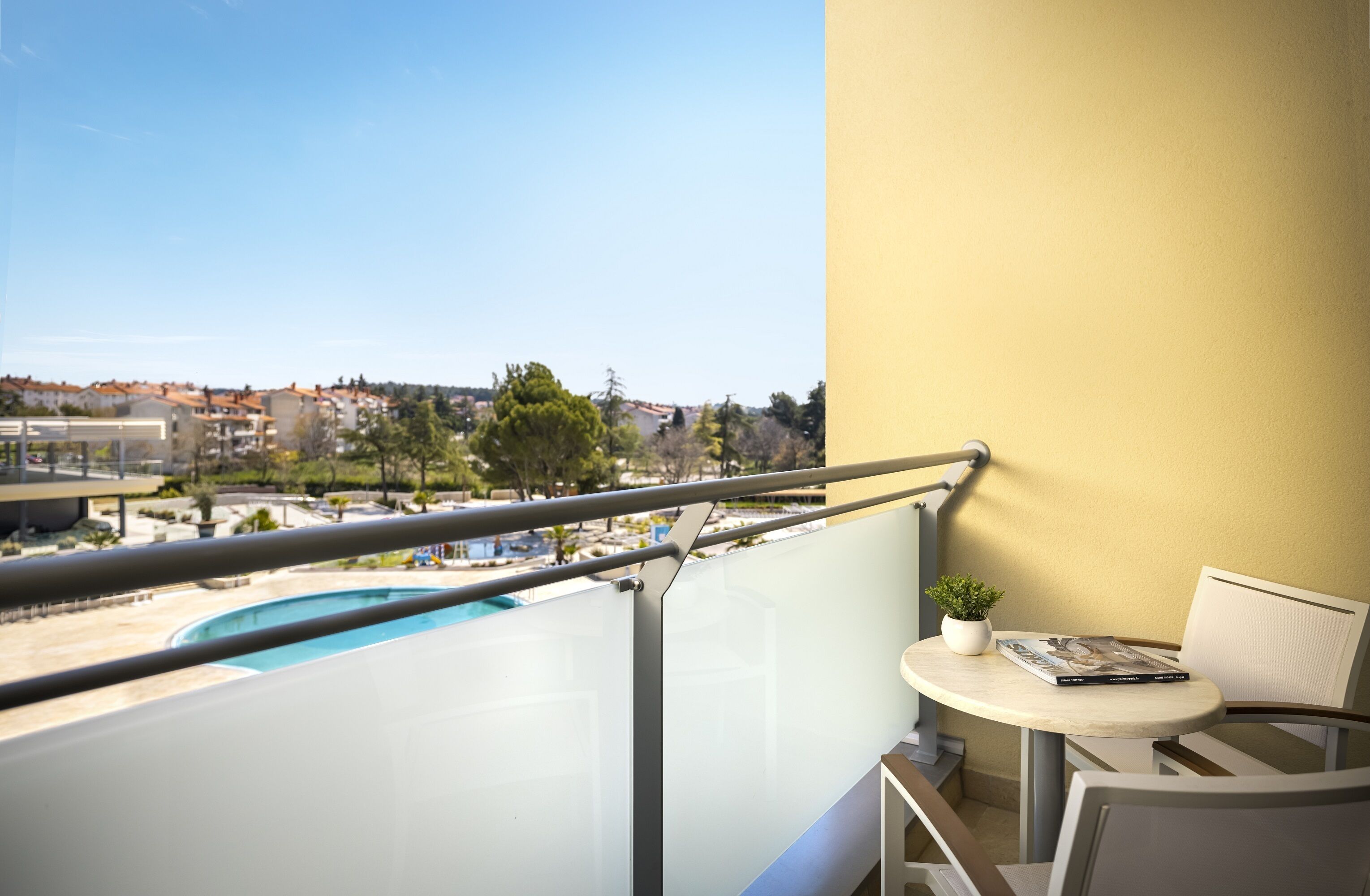 Un balcon offrant une vue dégagée sur une piscine, une petite table avec une plante et une chaise.