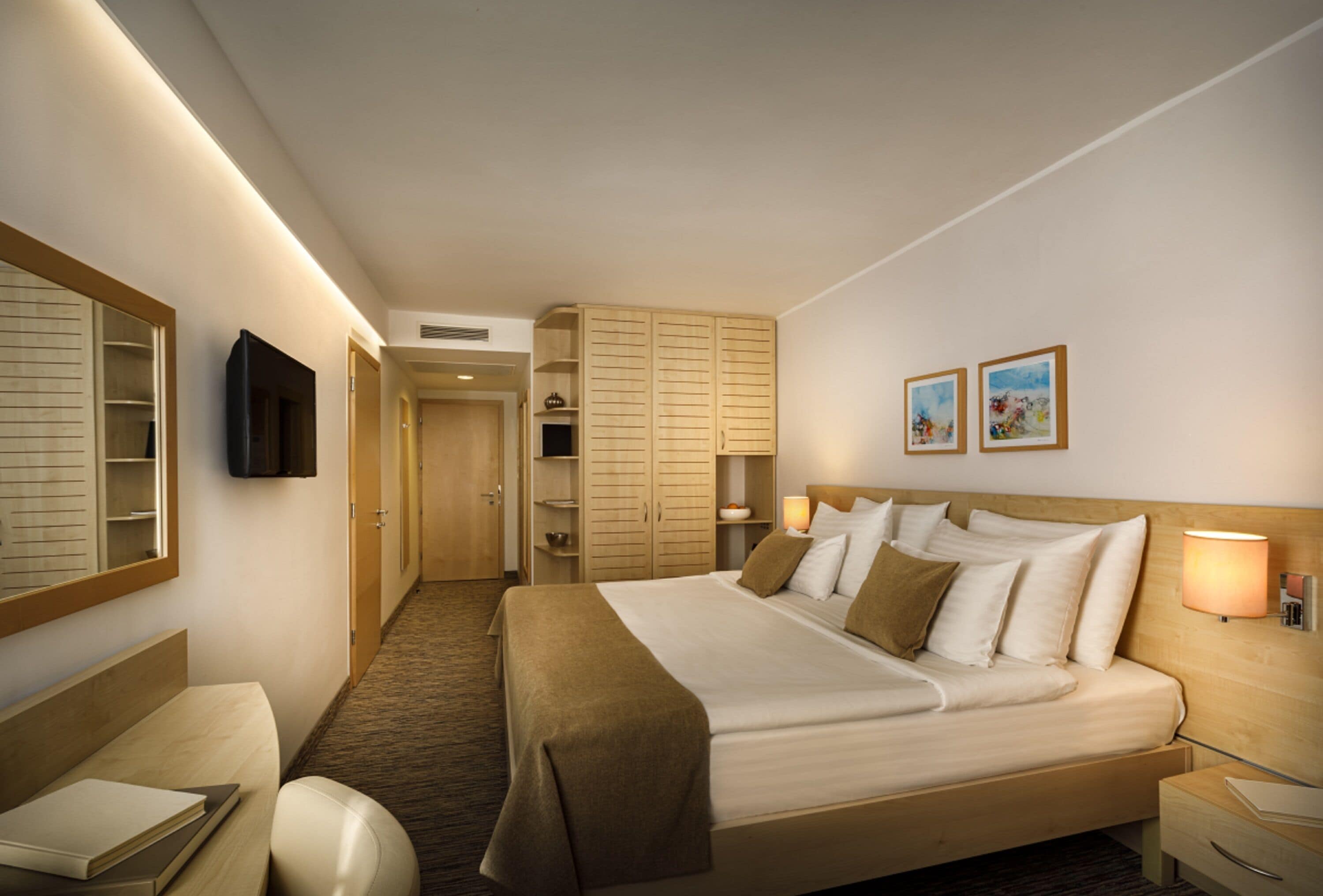 A hotel room with a large bed, a desk, a chair, a wardrobe, and a TV on the wall.
