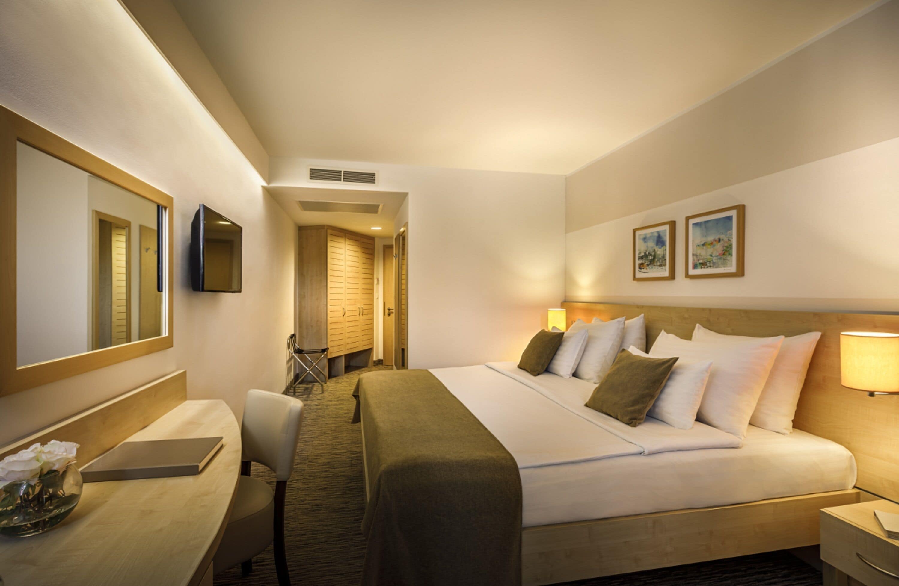 Habitación de hotel con una cama grande, un escritorio con silla, una mesita de noche, un espejo y un televisor montado en la pared.