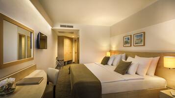 Habitación de hotel con una cama grande, un escritorio con silla, una mesita de noche, un espejo y un televisor montado en la pared.