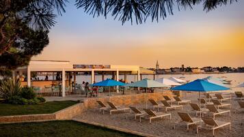 A beachfront restaurant with outdoor seating and umbrellas, overlooking the sea.