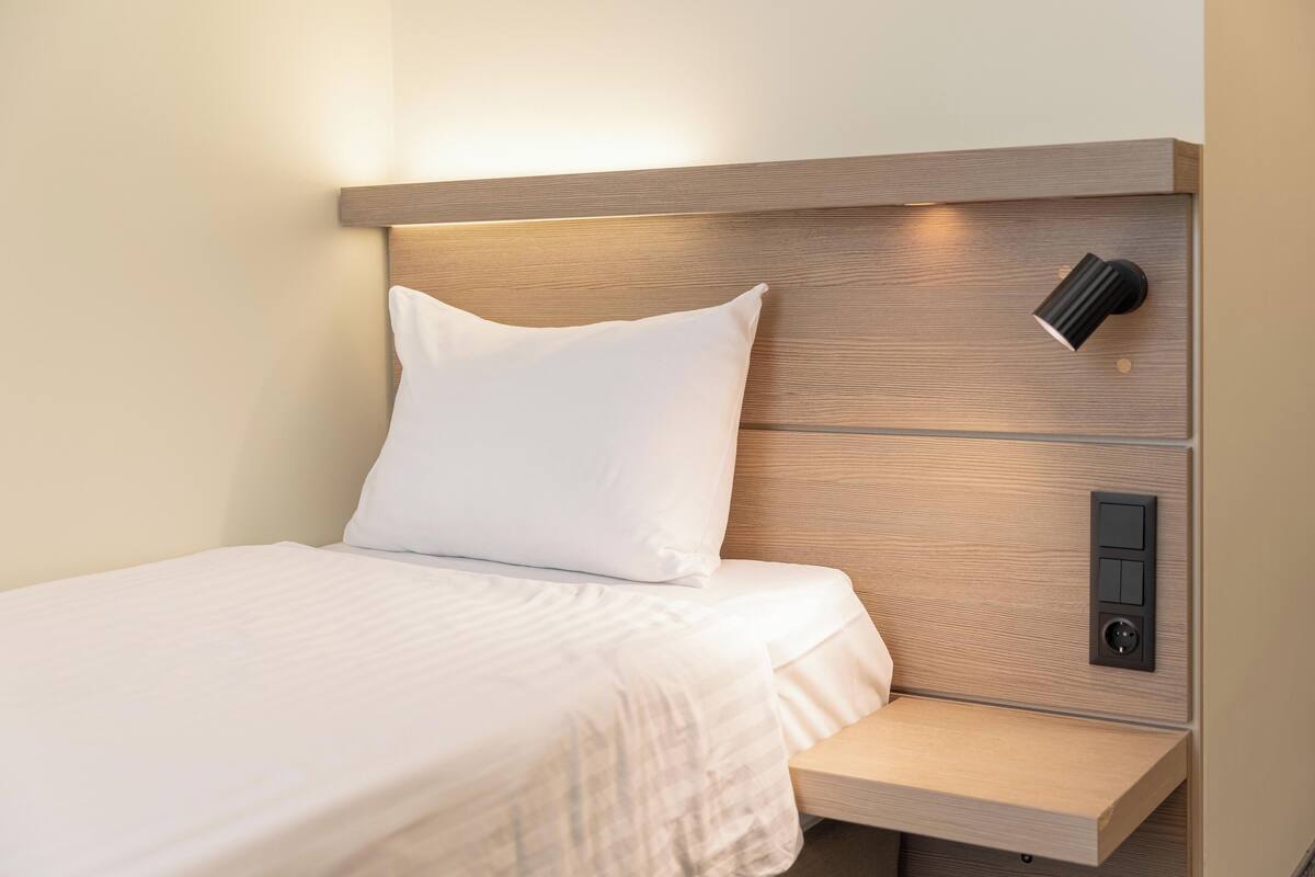 Una habitación de hotel moderna con cabecera de madera, una mesita de noche y luz integrada.