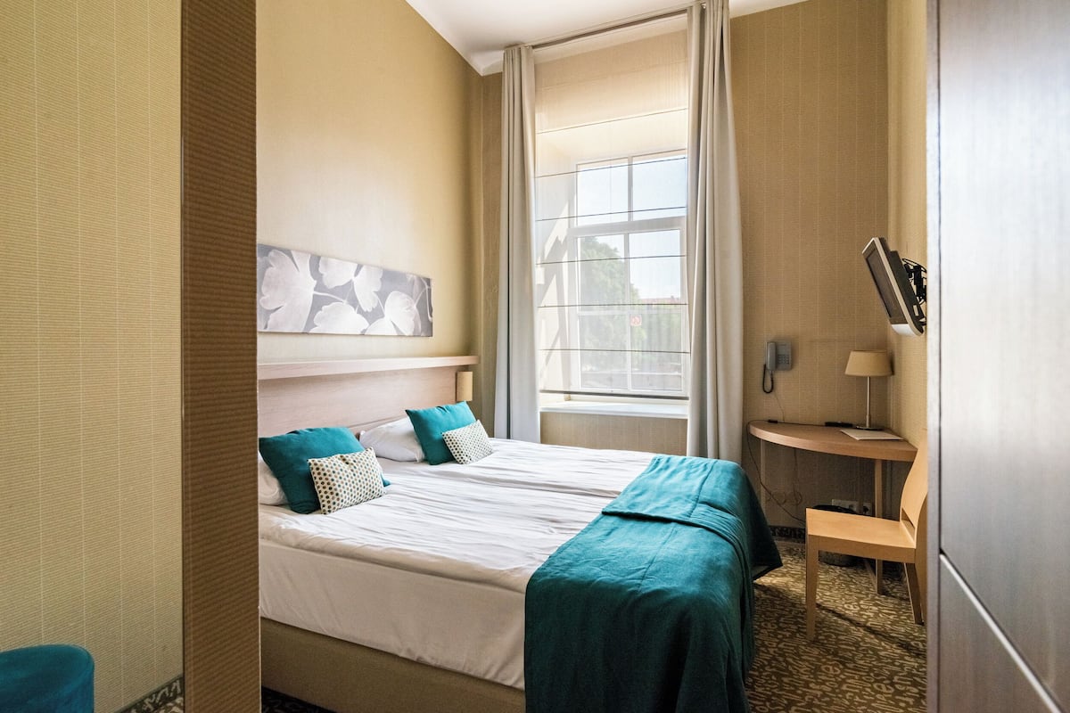 Habitación de hotel con cama, escritorio, silla, ventana y teléfono en la pared.