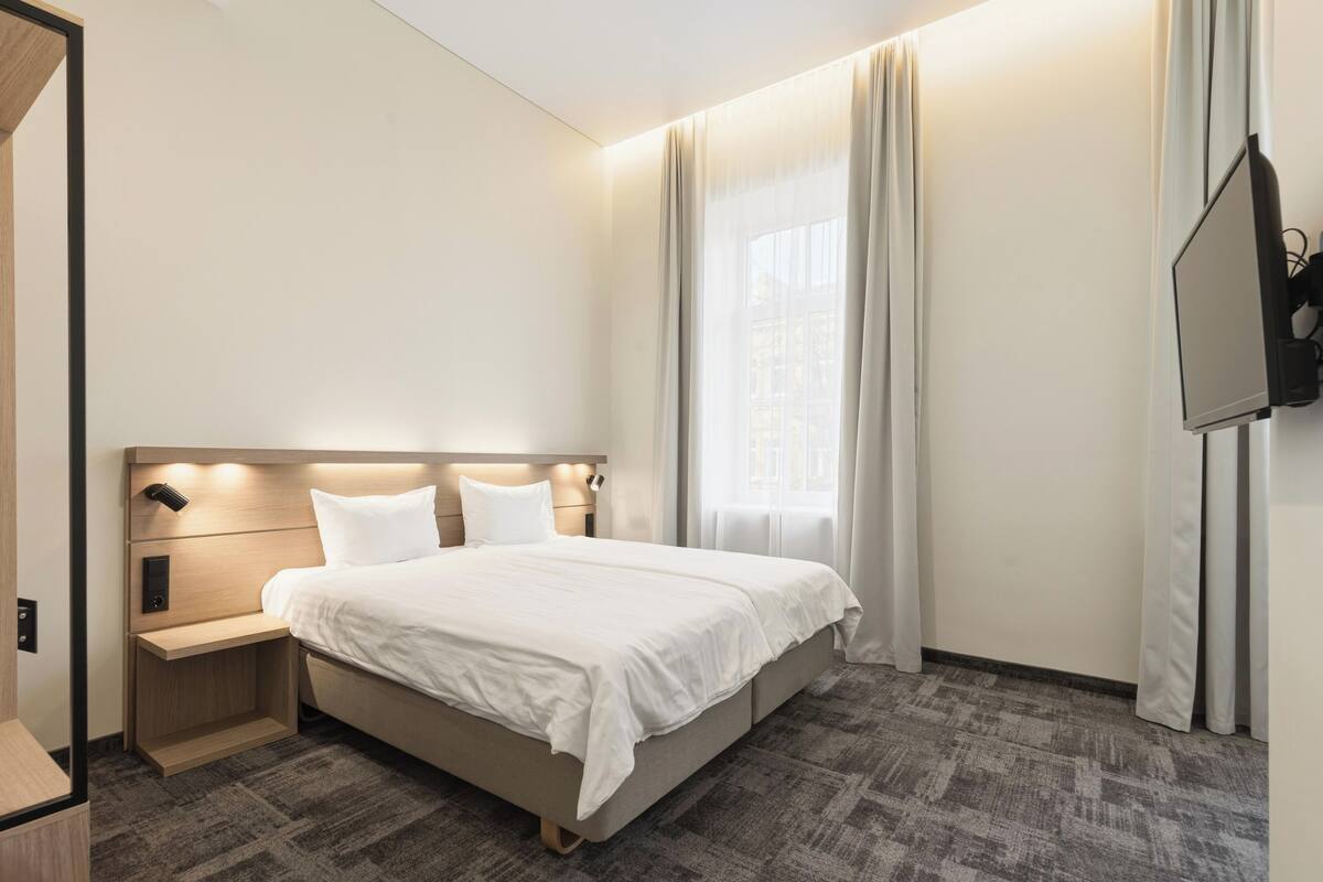 Una habitación de hotel con una cama, una mesita de noche y un televisor montado en la pared.