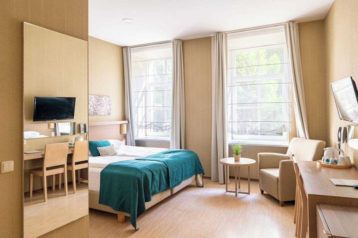 Una habitación de hotel con cama, escritorio, silla, televisión y ventanas amplias.