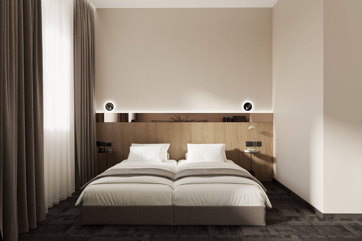 Una habitación de hotel moderna con una cama grande, cabecera de madera y una mesita de noche con lámpara.