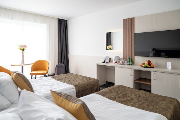 A hotel room with two beds, a desk with a flat-screen TV, a small table with a vase, and a chair.