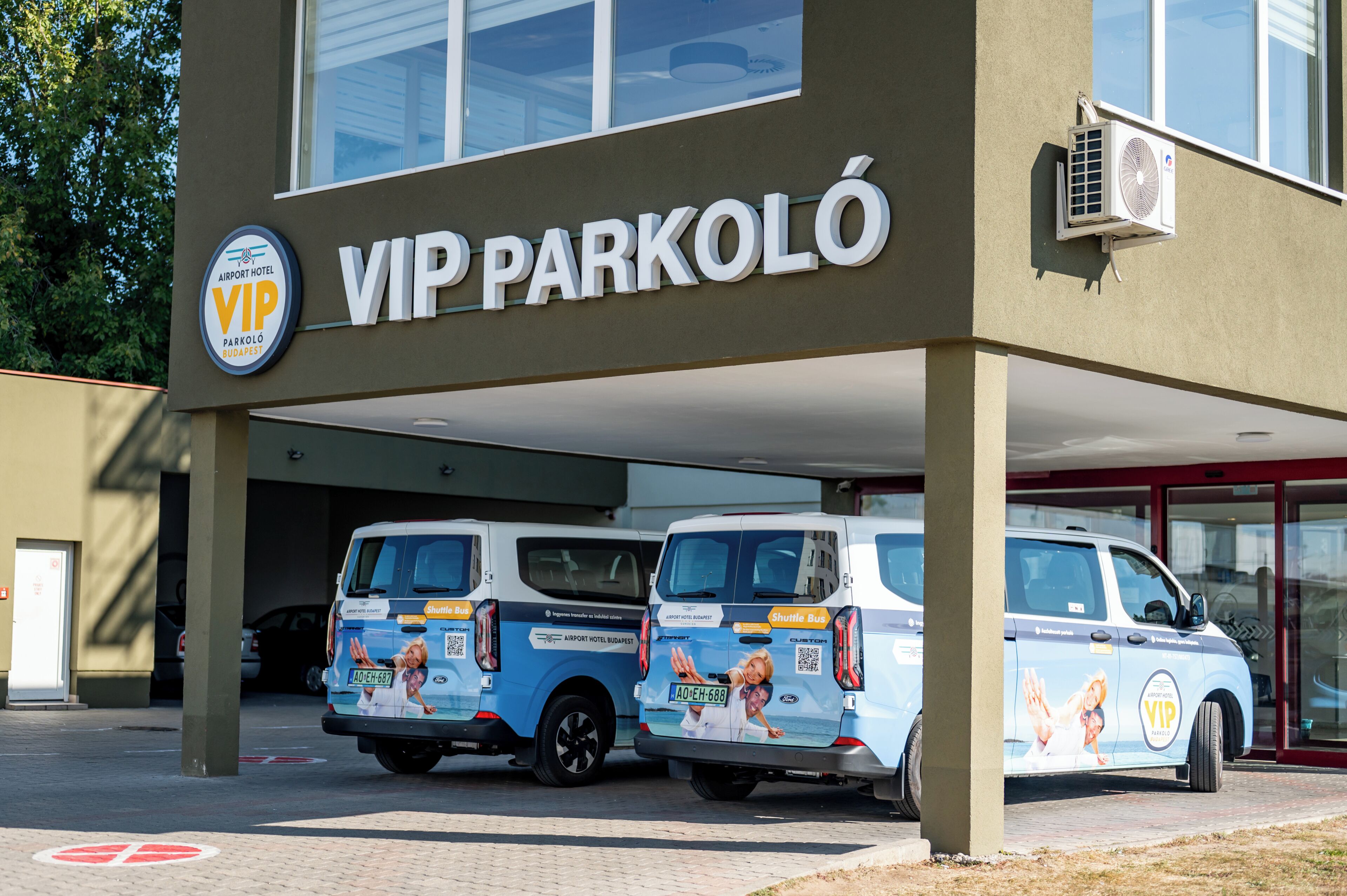 A building with a sign reading 'VIP PARKOLÓ' and two shuttle buses parked in front.