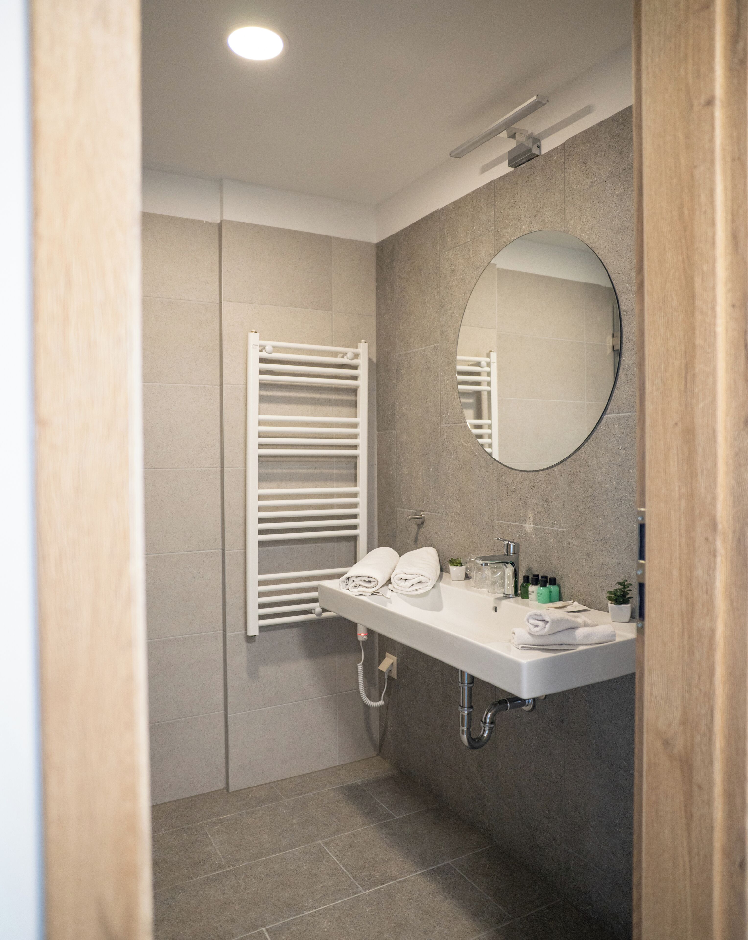 Un bagno moderno con lavandino bianco, specchio, porta asciugamani e doccia.