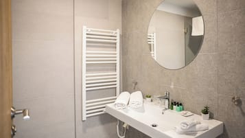 Un bany modern amb un envell, un mirall, un suport per tovalloles i una petita planta en test.