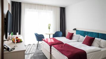A hotel room with a bed, bedside table, chair, and a small table with a vase of flowers.