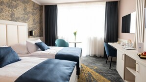 A hotel room with two beds, a desk, a chair, a small table with a vase, and a large window with curtains. - Airport Hotel Budapest (Vecsés)