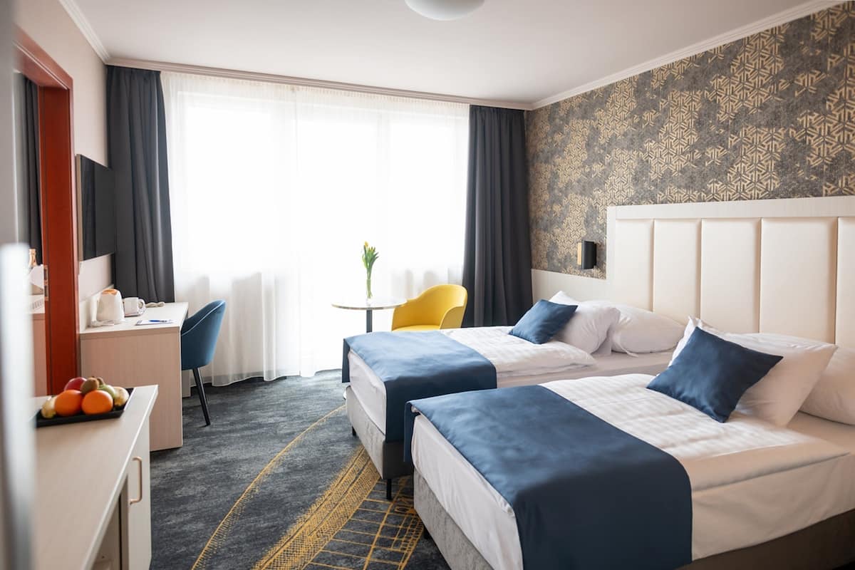 Habitación de hotel con dos camas, un escritorio, una silla y una pequeña mesa con una planta.