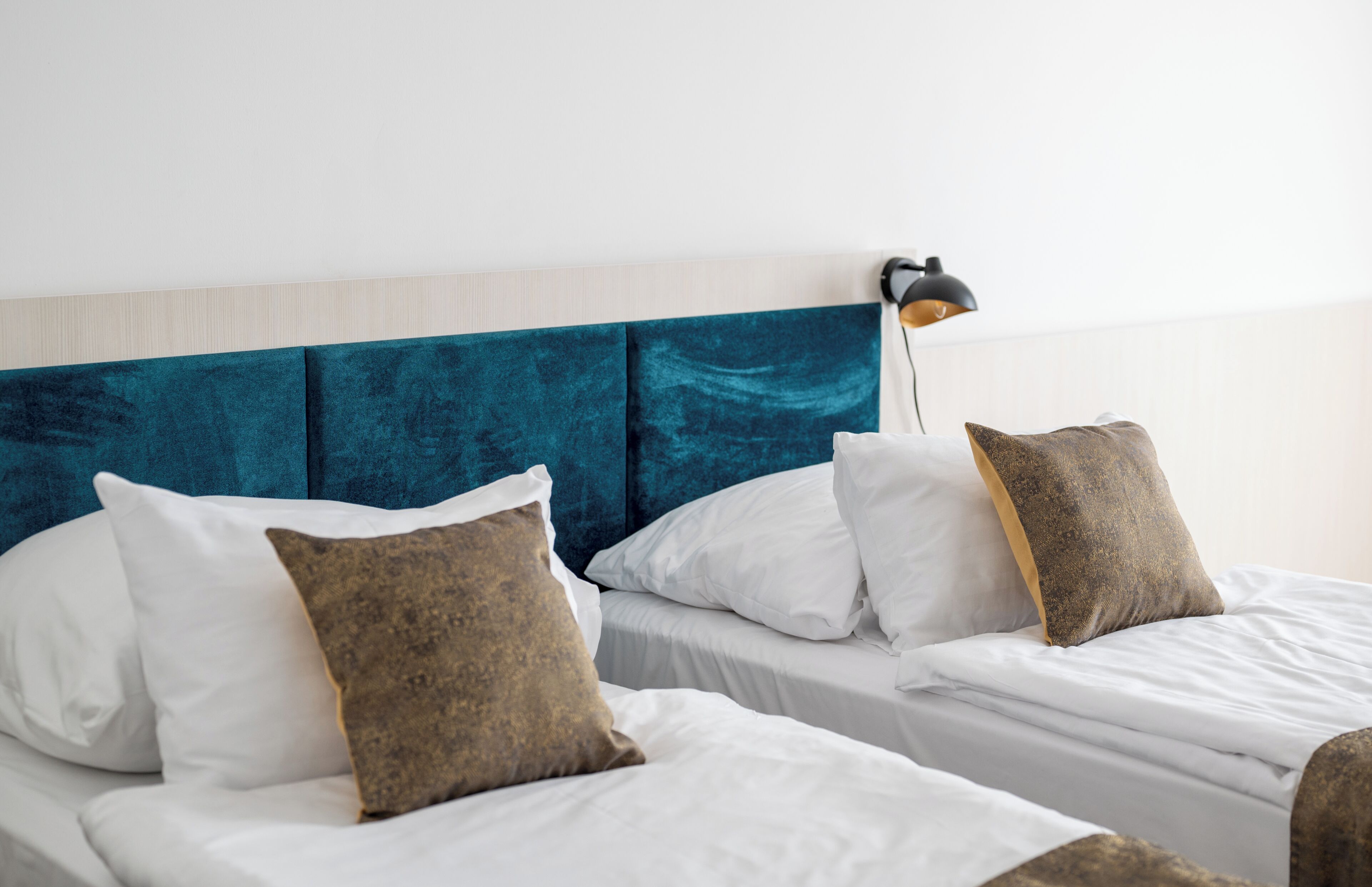 A hotel room with two beds, white bedding, teal headboard, and a bedside lamp.