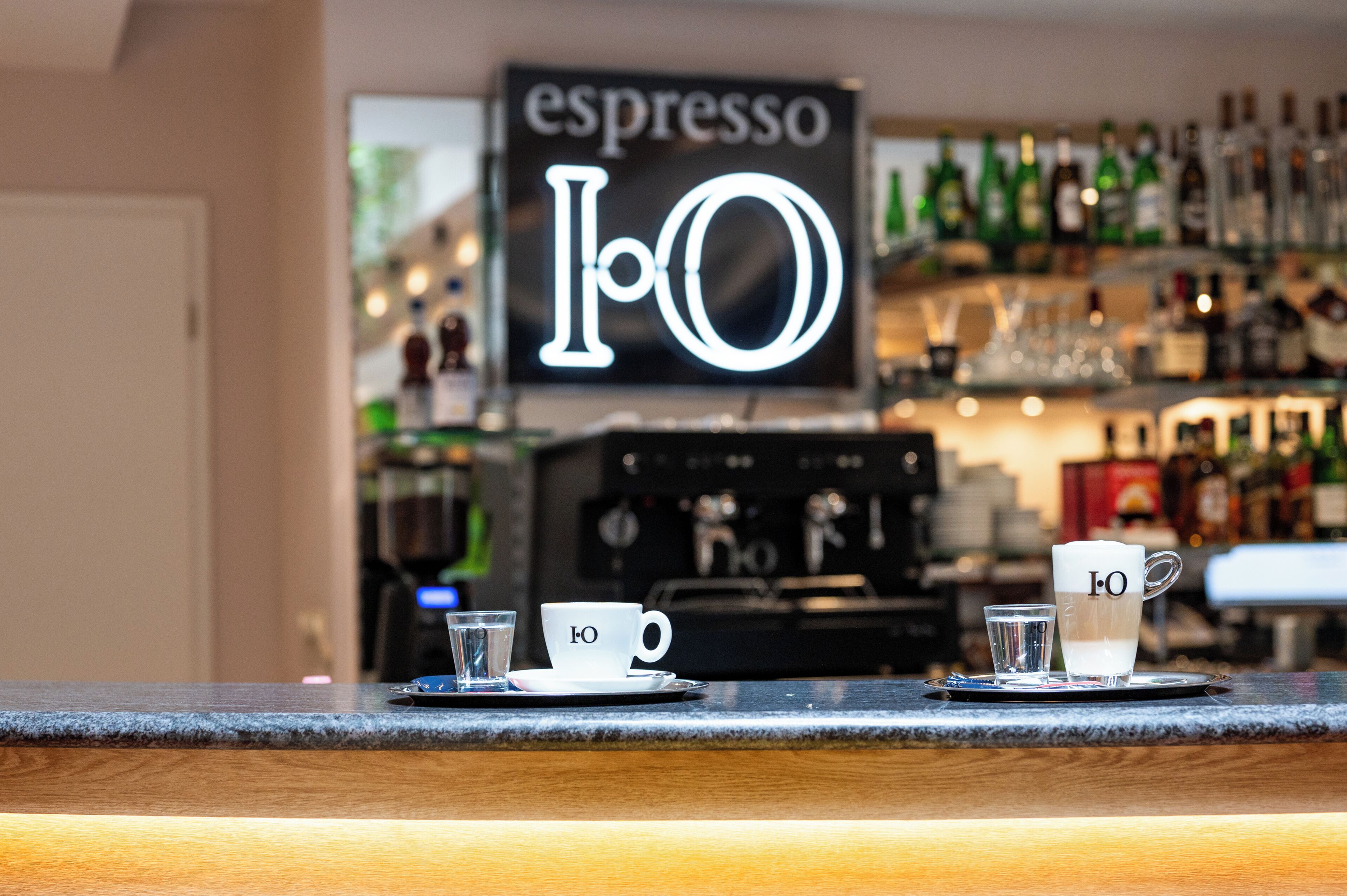 Un espace bar équipé de machines à expresso et d’une enseigne indiquant « expresso I.O. ».