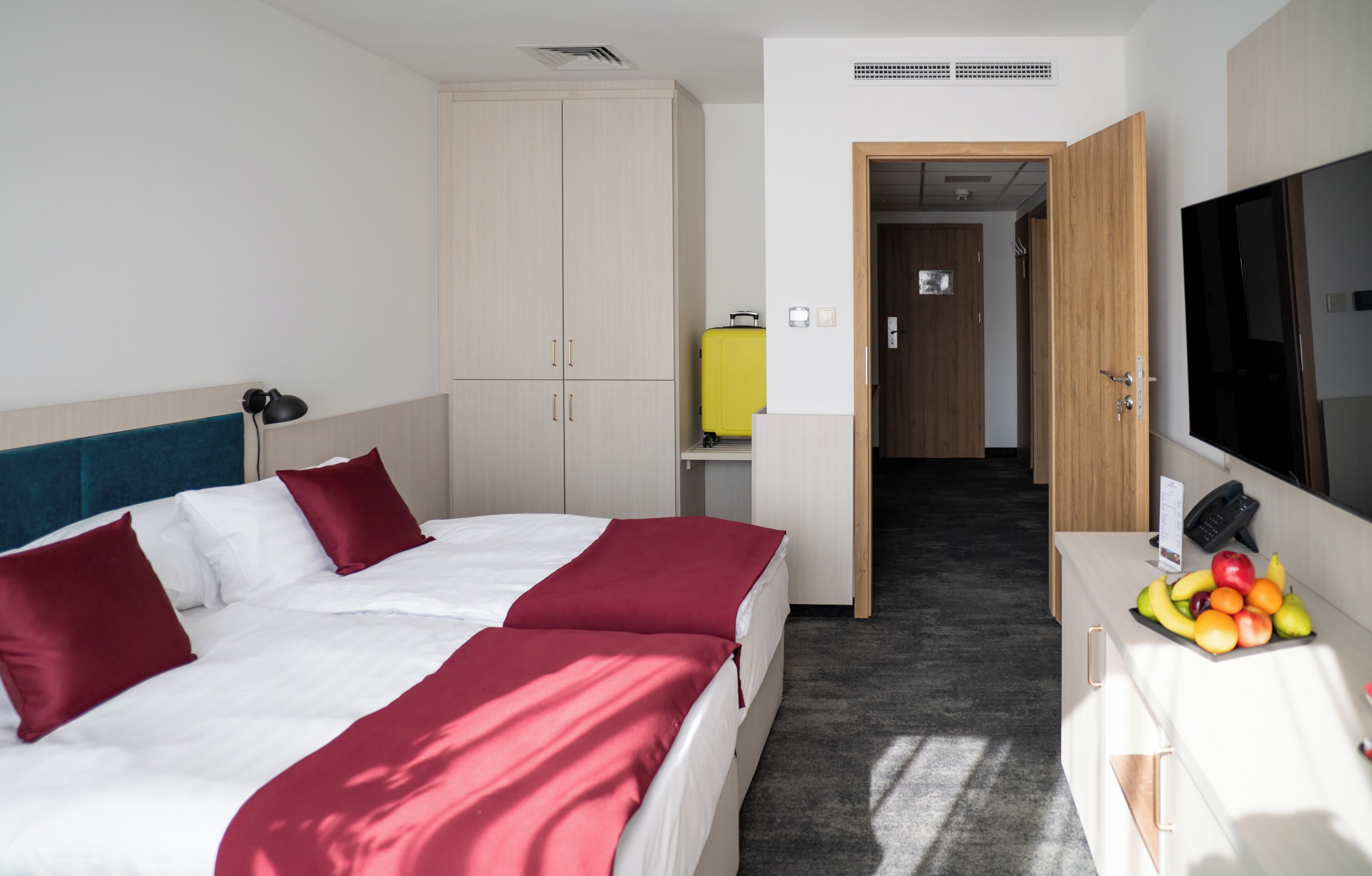 Habitación de hotel con cama, armario, escritorio, televisor y fruta en la mesita de noche.