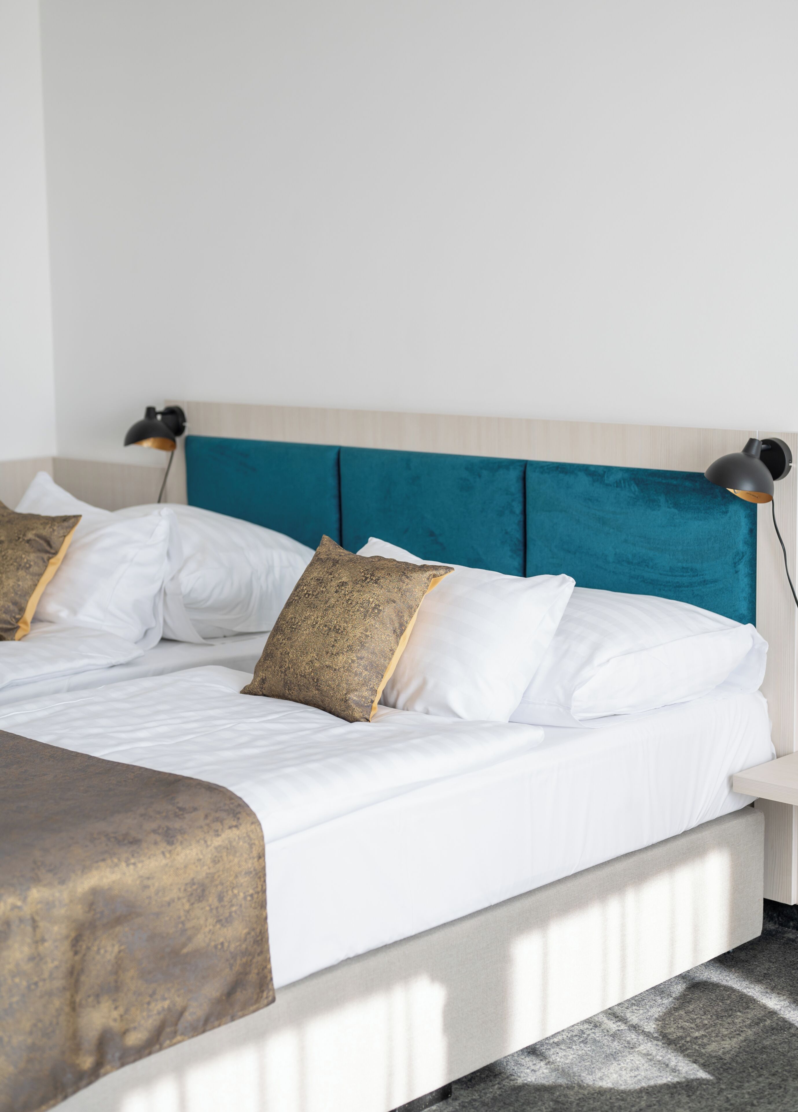 A neatly made bed with white linens and a teal headboard, two bedside lamps, and a brown throw blanket.