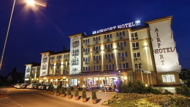 A multi-story building with "AIRPORT HOTEL" signage, a conference room, and a parking area with potted plants. - Airport Hotel Budapest (Vecsés)