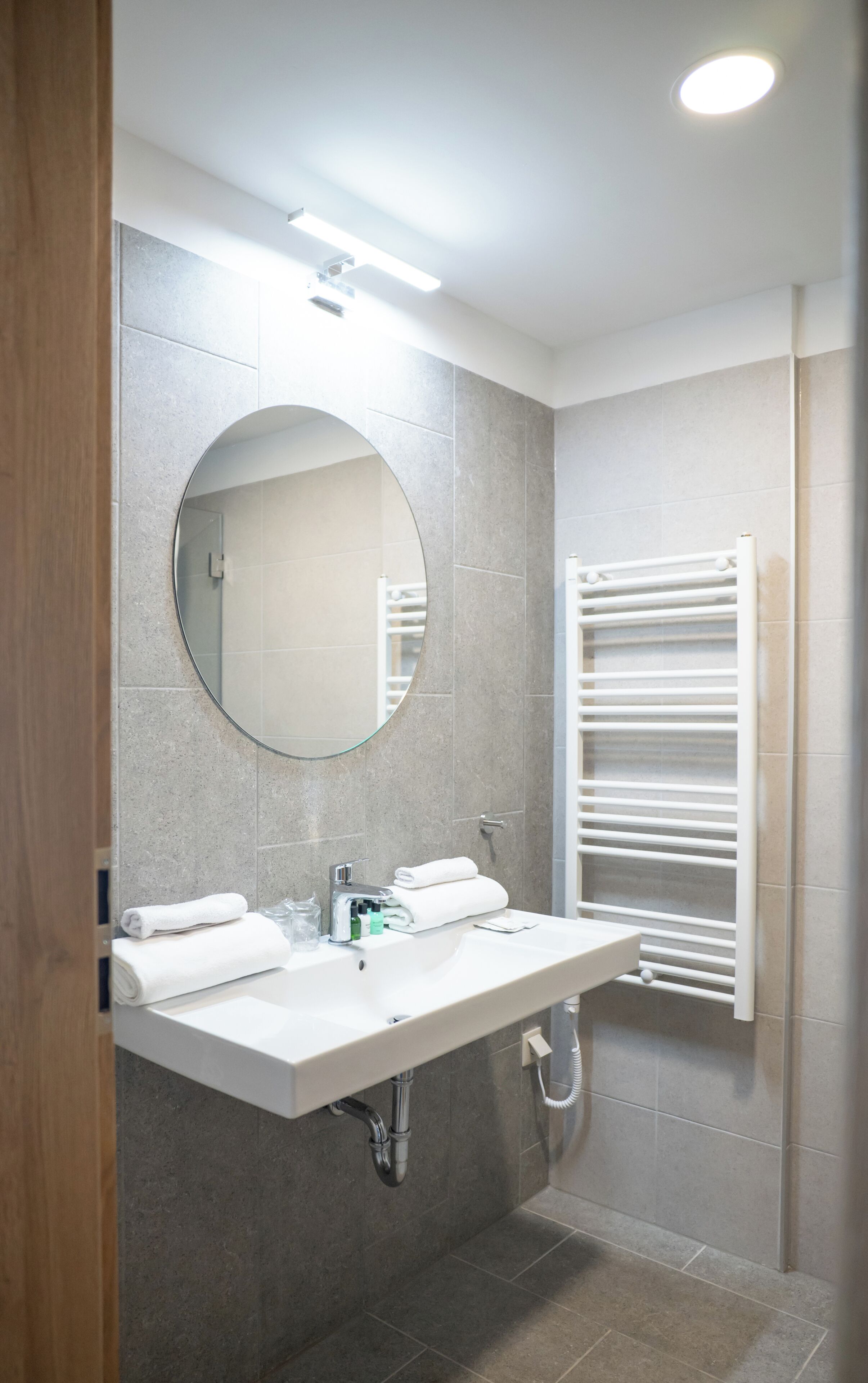 A modern bathroom with a large mirror, a white sink, and a towel rack.