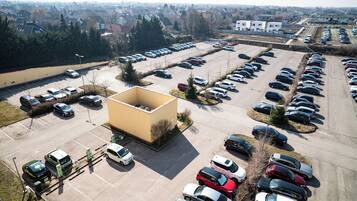 Vista aérea de un estacionamiento con múltiples filas de coches aparcados, un pequeño edificio y zonas residenciales circundantes.