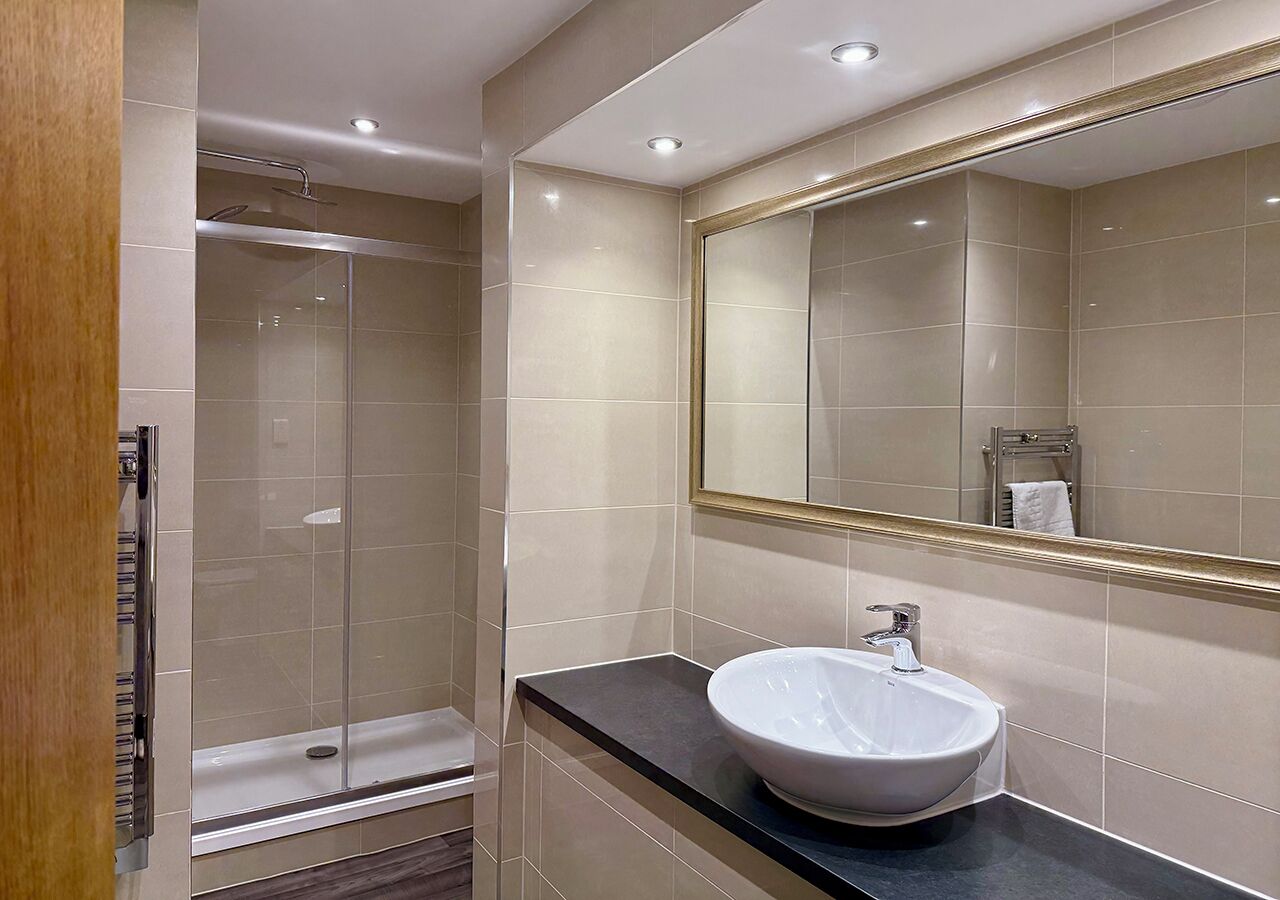 Un baño moderno con cabina de ducha de vidrio, un lavamanos blanco y un espejo grande.