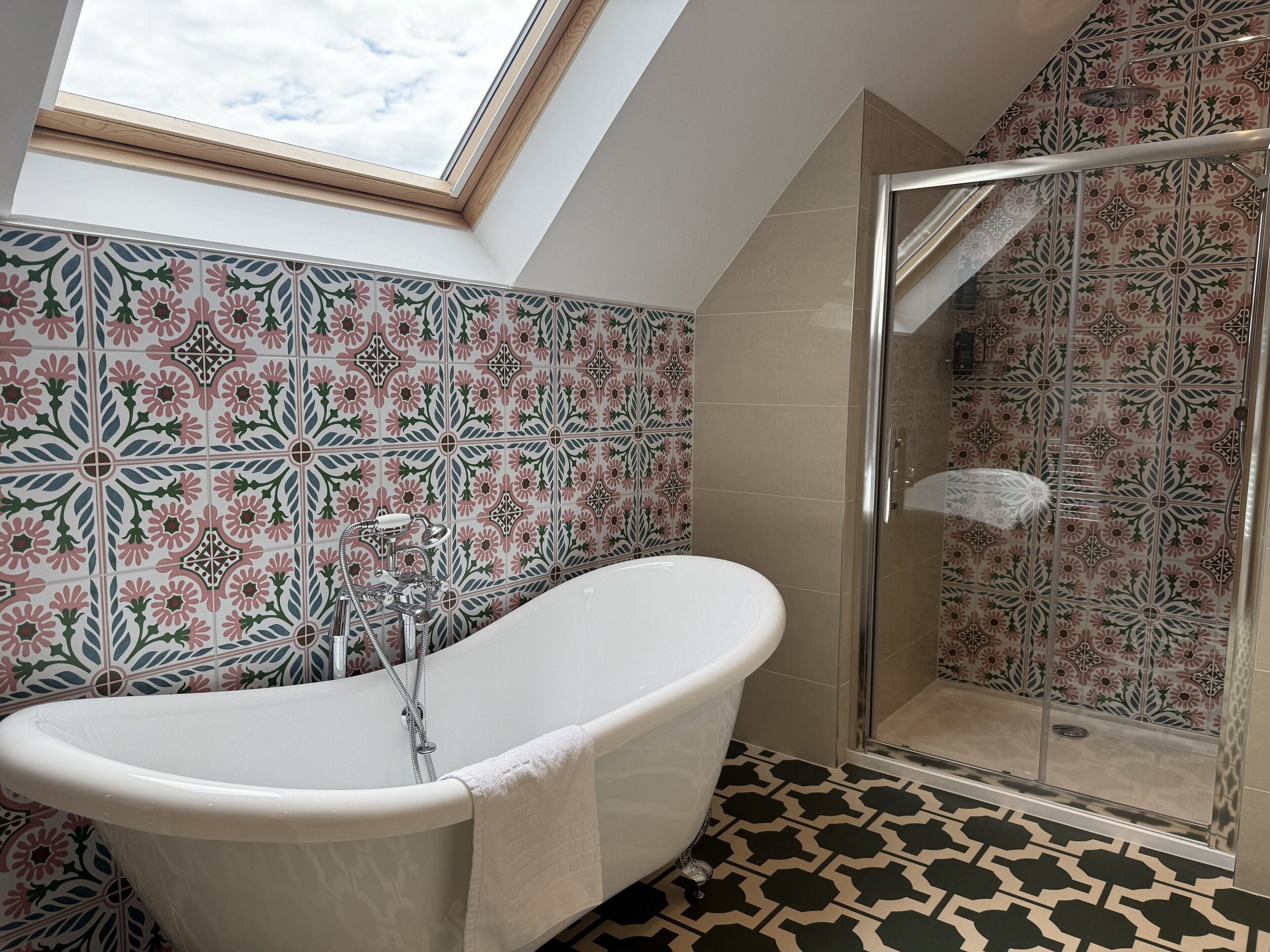 A bathroom with a freestanding bathtub, a shower enclosure, and a skylight.