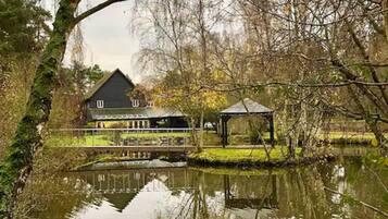 Een huis met een ruime veranda en een tuinhuisje bij een vijver.