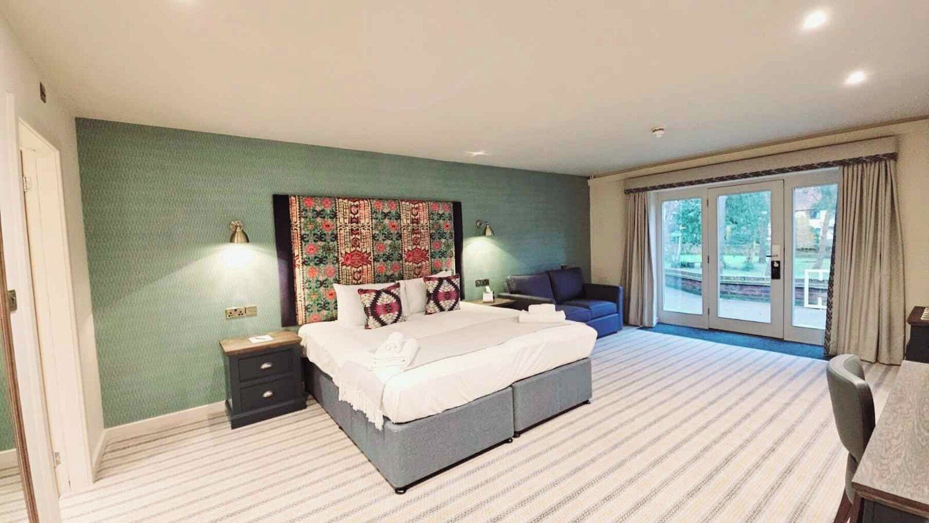 A bedroom with a large bed, a nightstand, a desk, and a view of the outdoors through a sliding glass door.