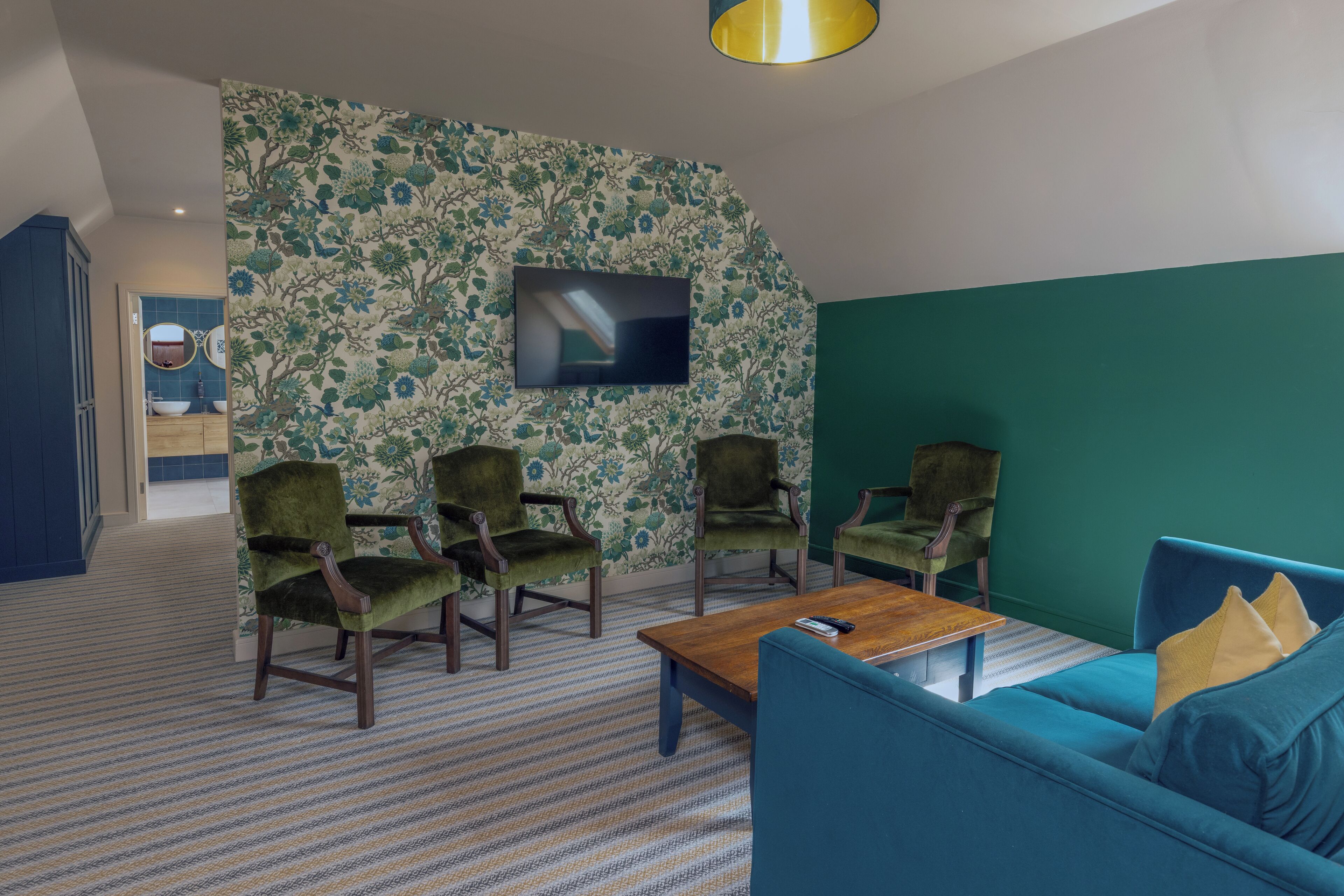 A living room with a TV, green armchairs, a blue sofa, and a patterned carpet.