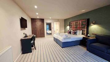 A hotel room with a bed, a desk, a chair, a sofa, and a large tapestry on the wall.