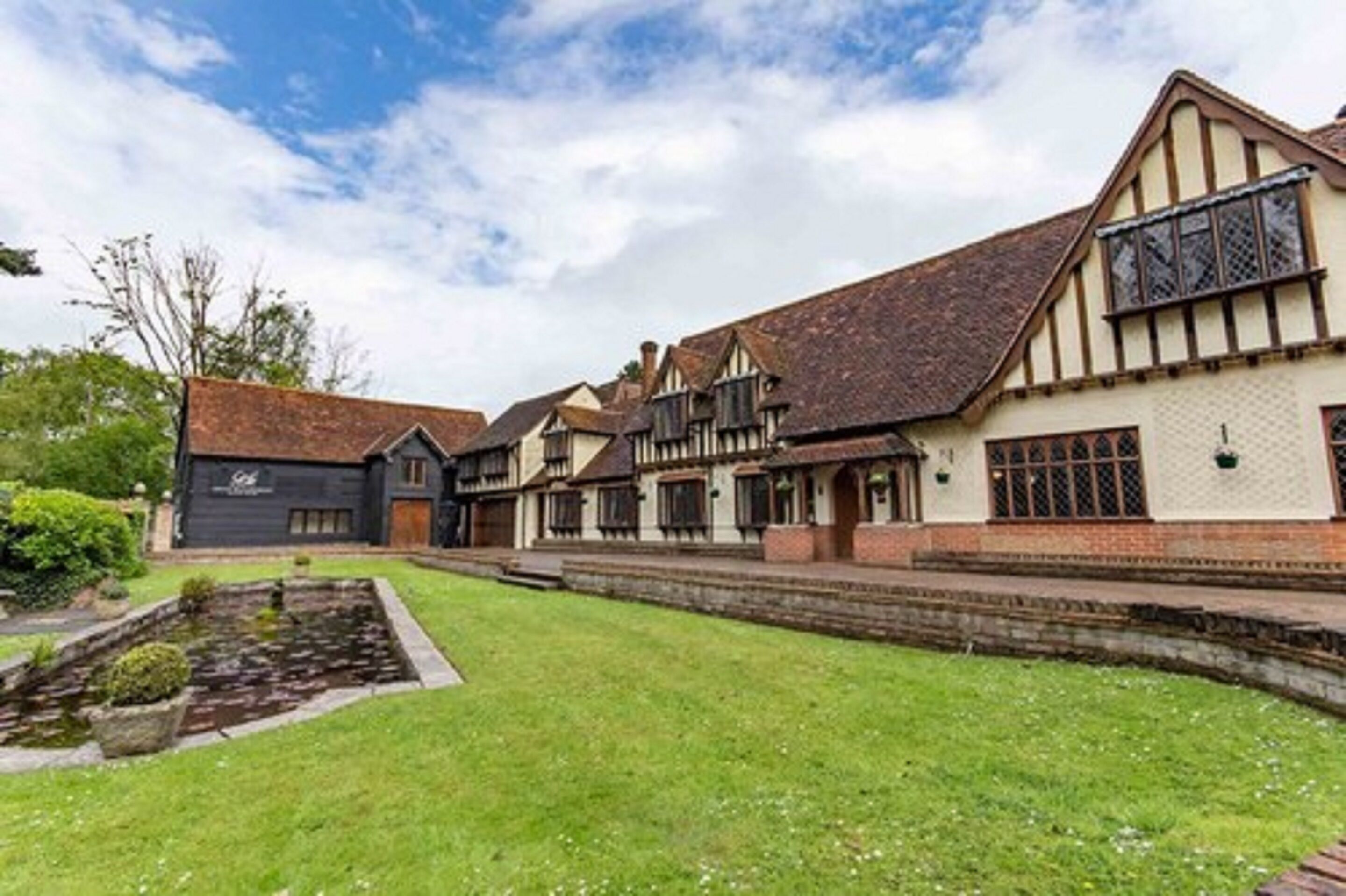 A traditional Tudor-style building with a symmetrical facade, a central entrance, and a small garden with a pond.