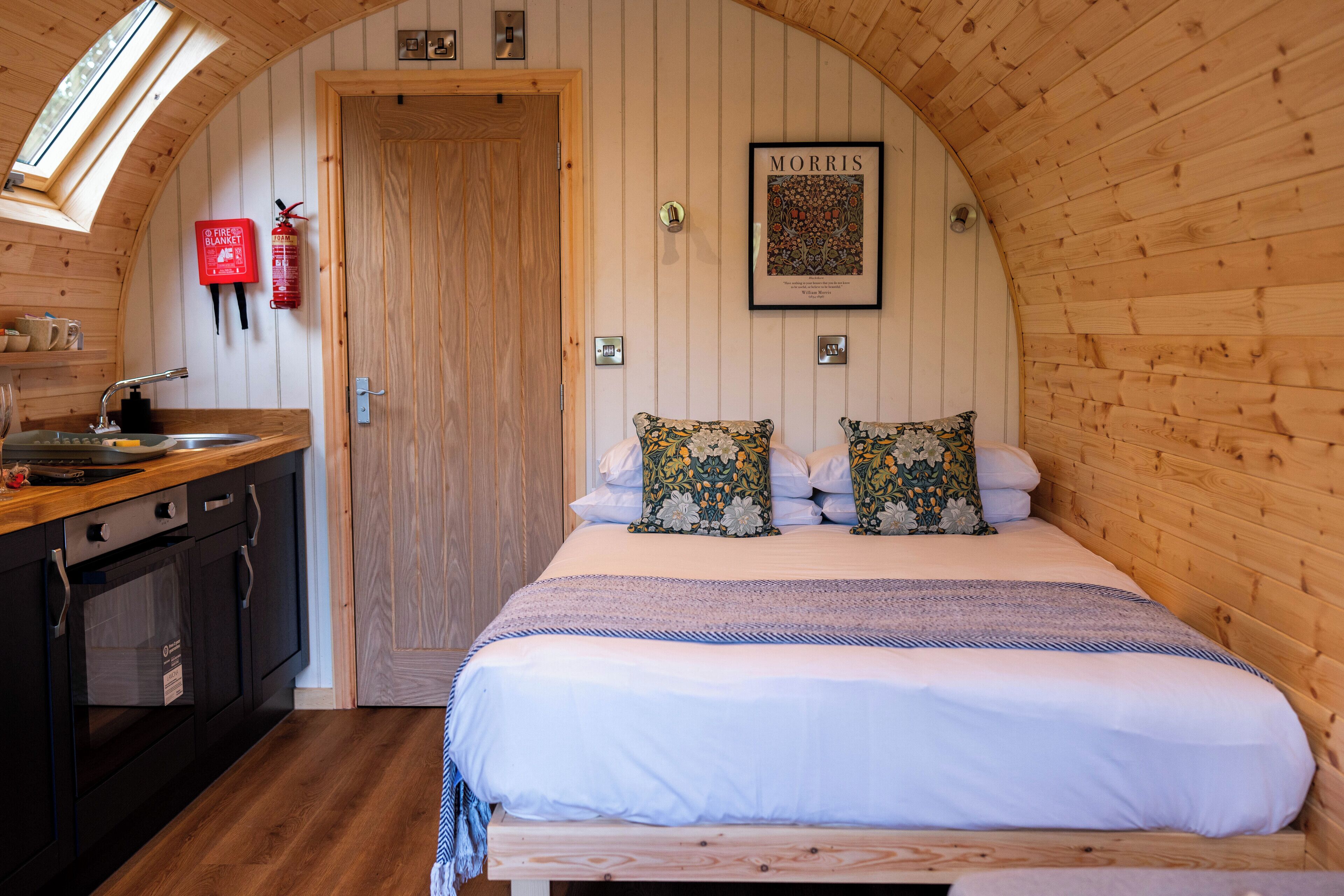 A cozy, wooden-paneled room with a bed, a small kitchen area, and a fire extinguisher on the wall.