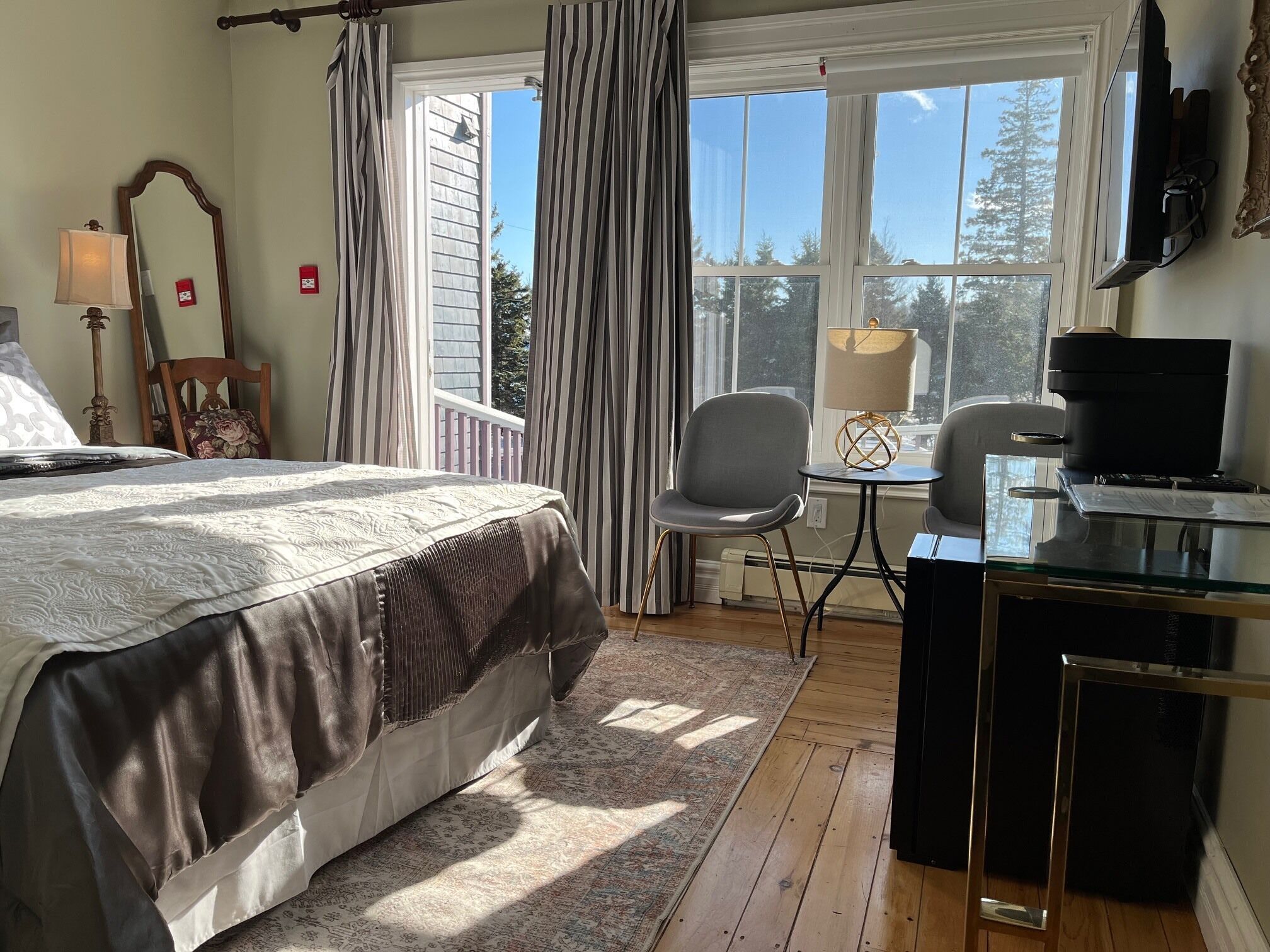 A bedroom with a bed, a desk, a chair, a TV, and a window with curtains.