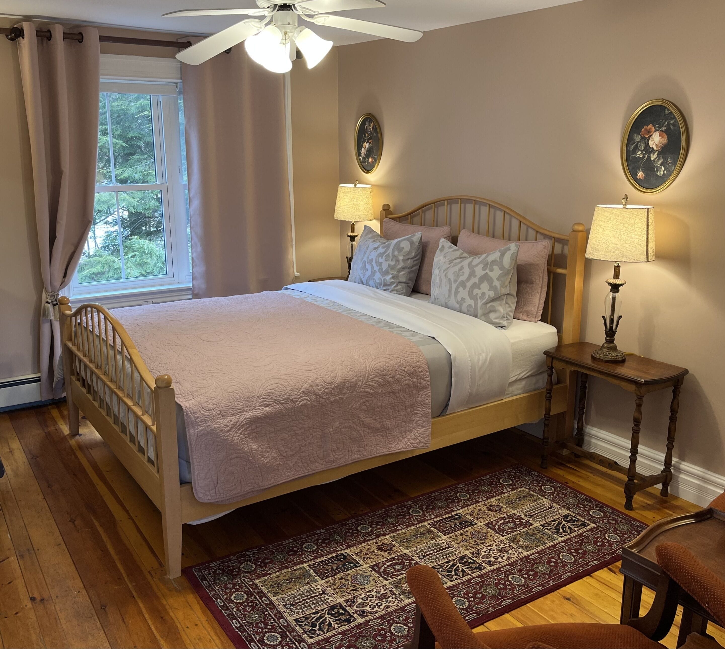 A bedroom with a wooden bed, a nightstand, a floor lamp, a patterned rug, and a window with curtains.