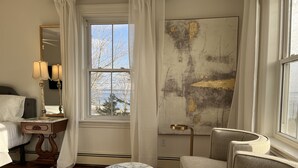 A hotel room with a bed, a marble-topped table, a chair, a large abstract painting, and a window with a view of trees and a building. - Surfside Inn (Queensland)