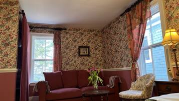 A room with floral wallpaper, a red sofa, a chair, a bed, and a window with curtains.