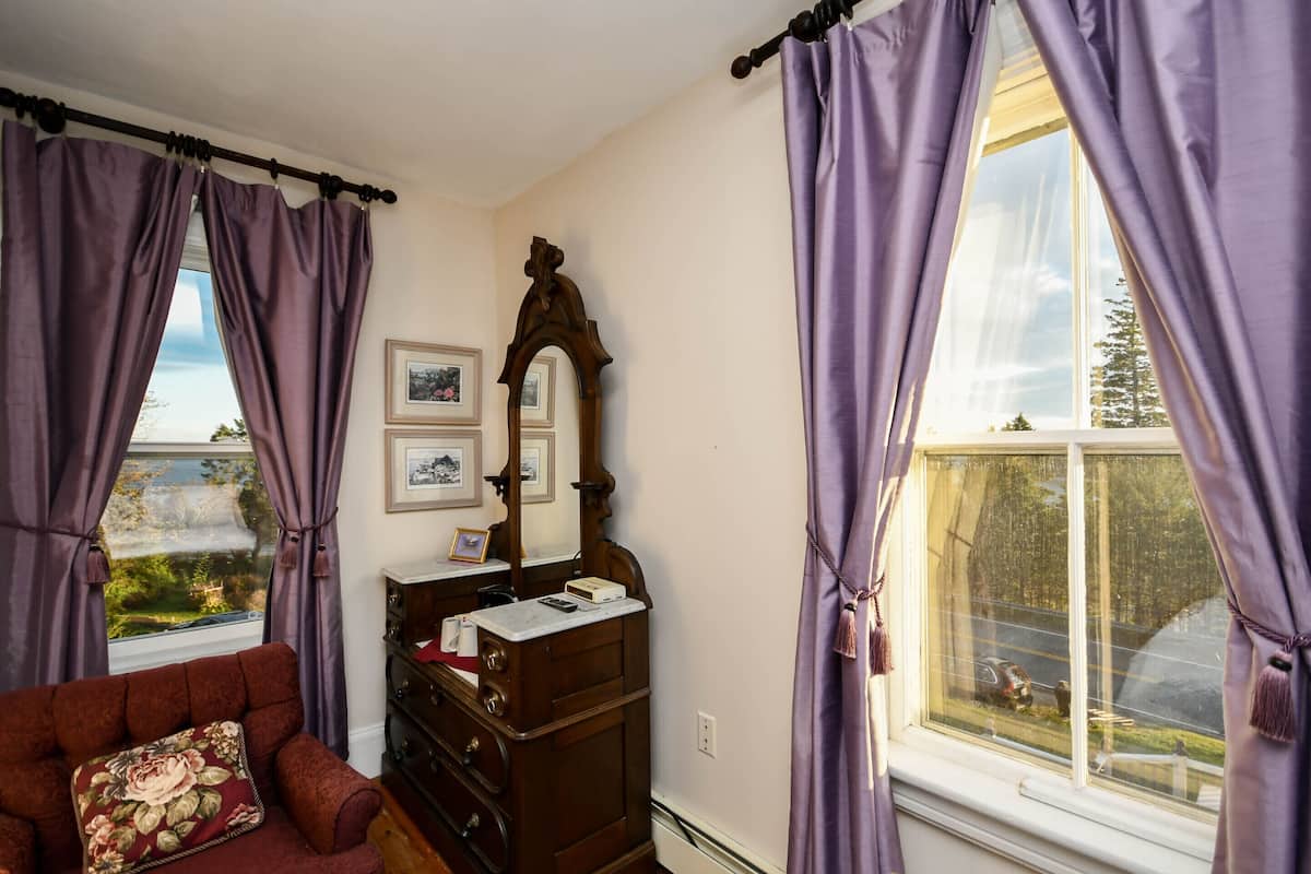 A room with a view of a body of water, a wooden dresser, a mirror, and a red sofa.