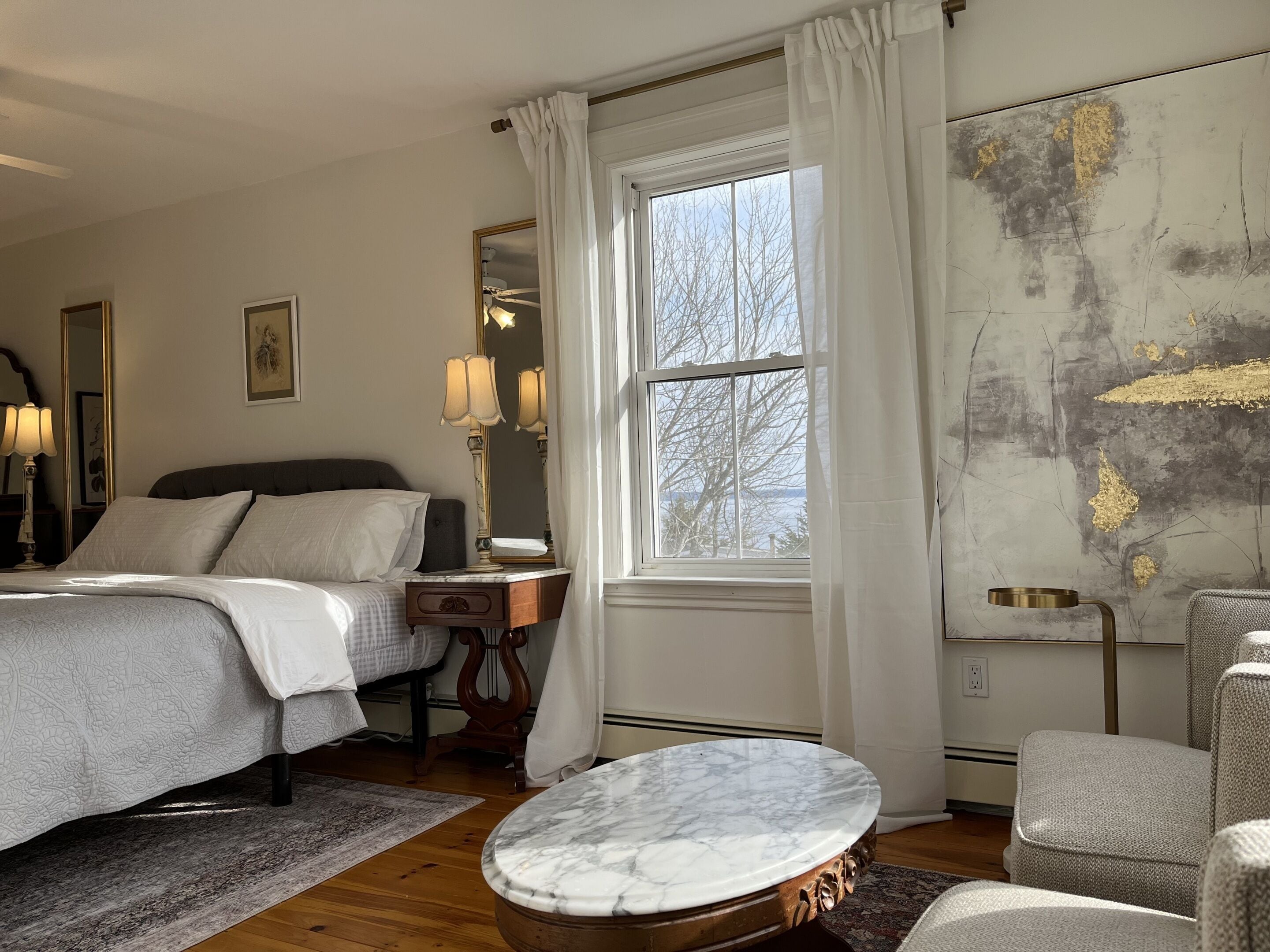 Une chambre à coucher comprenant un lit, une table de chevet, une lampe, un miroir, une fenêtre et une table basse en marbre.