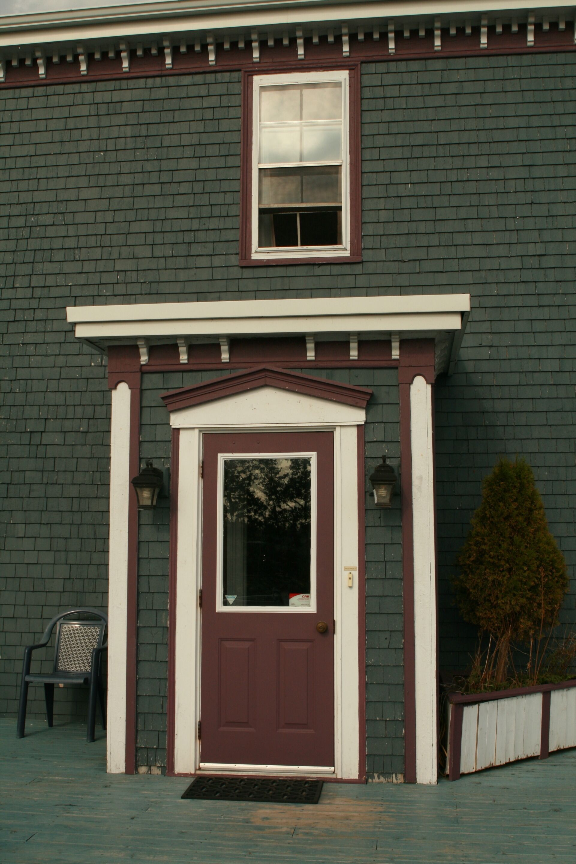 Una casa con fachada verde oscuro, una puerta roja y una ventana con marco blanco sobre la puerta.